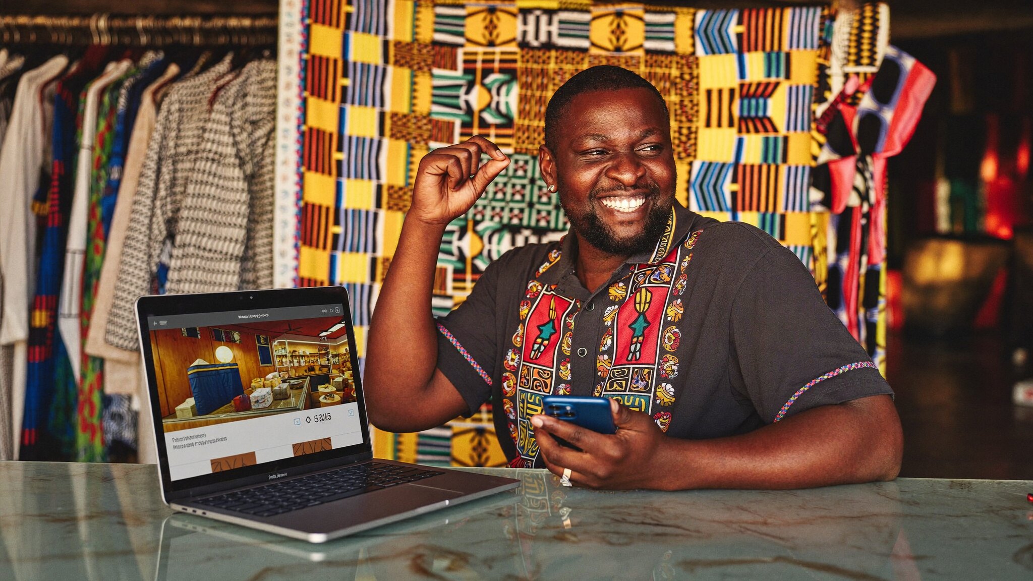 Rwandan shop owner replying to customers on WhatsApp with his website open on a laptop in a Kigali boutique